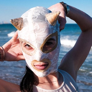 May include: A white lace mask with gold accents and a pointed top. The mask covers the eyes and nose, and has a lace design.