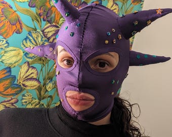 Dark purple stretchy fabric mask with spikes dotted with sequins and flower shaped pearls.