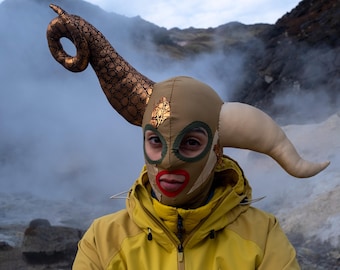 Striking face mask in earthy tones with asymmetrical horns.