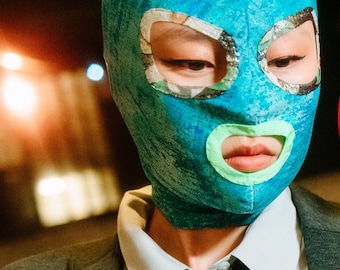 Turquoise shiny fabric mask with printed squared shape eye contours and neon green lips.