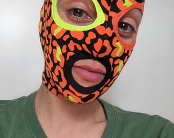 Funky orange print fabric mask with neon eye contours and black lips.