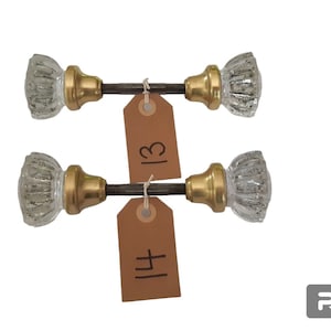 May include: Two sets of antique glass door knobs with gold metal accents. The knobs are attached to a metal rod. The knobs are labeled with the numbers 13 and 14.