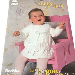 May include: A vintage baby knitting pattern book titled "Beehive Baby Talk" featuring a baby in a white knitted dress and shoes. The baby is seated on a pink chair. The book cover has the text "le Jargon de Bébé".