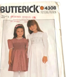 May include: Vintage sewing pattern for children's dresses. The pattern is for a white dress with puffed sleeves and a pink dress with polka dots. The pattern is from Butterick and is number 4308.