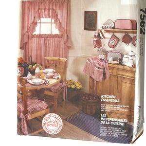 May include: A McCall's Home Decorating pattern envelope showing a kitchen scene with red and white gingham curtains, a table setting, and kitchen essentials. The text includes "Kitchen Essentials" and "Les Indispensables de la Cuisine."