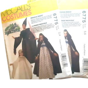 Puede incluir: Tres sobres de patrones de disfraces McCall's con diseños de disfraces medievales. Los sobres muestran imágenes de mujeres con vestidos largos y capas, con texto que incluye "Medieval Magic" y números de patrón.
