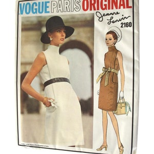 Könnte beinhalten: Vintage Vogue Paris Original Schnittmuster. Das Bild zeigt eine Frau in einem weißen Kleid mit schwarzem Gürtel und Hut sowie eine Zeichnung eines braunen Kleides. Der Text "Vogue Paris Original" ist sichtbar.