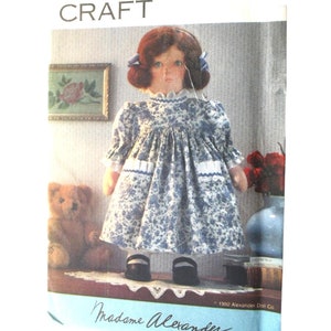 May include: A Vogue Craft sewing pattern envelope, number 8494, featuring a doll with auburn hair wearing a blue and white floral print dress with ruffled pockets. The packaging includes the text Vogue Craft, 8494, and Madame Alexander.