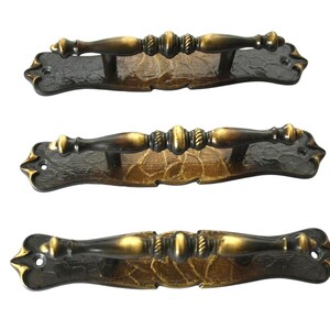 May include: Three horizontal drawer pulls featuring a dark bronze finish with gold highlights. Each handle has a central grip with decorative rope-like detailing and a textured, leaf-patterned backplate with two screw holes for mounting.