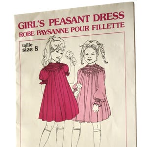 May include: Vintage sewing pattern for a girl's peasant dress, size 8. The cover features an illustration of two girls wearing pink dresses. The text reads "GIRL'S PEASANT DRESS" and "ROBE PAYSANNE POUR FILLETTE". The pattern is from Grace L. Knott Smocking Supplies Ltd.