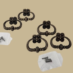 May include: Set of five antique gold-toned cabinet drawer pulls with ornate designs. Each pull has a ring-shaped handle and a decorative floral pattern. The set includes two screws for each pull.