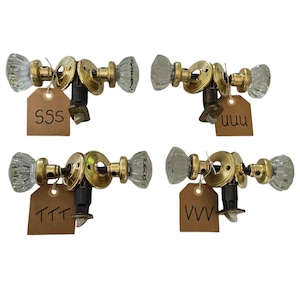 Peut inclure: Quatre boutons de porte en laiton antique avec des boutons en verre transparent. Chaque bouton est étiqueté avec une étiquette brune : SSS, TTT, UUU et VVV.