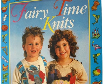 May include: A softcover book titled Fairy Time Knits by Amy Carroll and Denise Brown. The cover features two children wearing patterned knit sweaters, surrounded by a blue border decorated with small illustrations of fairy tale icons.