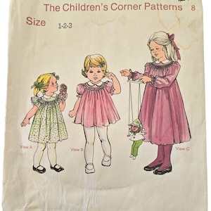 May include: A vintage sewing pattern for a girl's dress. The pattern is called "The Children's Corner Patterns" and is size 1-2-3. The pattern shows three different views of the dress, one with a green and white print, one with a pink print, and one with a solid pink print. The pattern is called "Mindy".