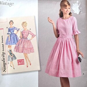 May include: Simplicity vintage sewing pattern for a 1960s dress. The pattern envelope features a pink dress with a belt and a model wearing the dress. The envelope also shows illustrations of the dress in different colours. The pattern size is U.S. 4-12.