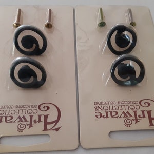 May include: Two packs of black swirl cabinet knobs with screws. Each pack contains two knobs and two screws. The packs are labelled "Artware Collections".