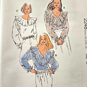 Könnte beinhalten: Ein Kwik Sew Schnittmusterumschlag 2248 für die Größen XS-S-M-L-XL. Die Vorderseite zeigt Illustrationen von drei Varianten einer langärmeligen Bluse mit großem Rüschenkragen. Der Text enthält Kwik Sew, Schnittmuster 2248 und Kerstin Martensson.