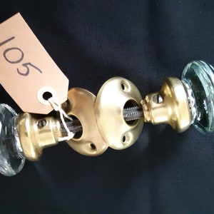 May include: A set of antique glass door knobs with brass accents. The knobs are clear glass with a textured surface and the accents are a shiny gold colour.