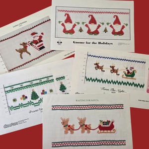 May include: A collection of Christmas cross-stitch patterns on white fabric. Designs include Santa Claus, reindeer, gnomes, Christmas trees, and gift boxes. The patterns are displayed on a red background.