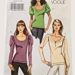 May include: A Very Easy Vogue sewing pattern envelope V8451, size AA (6-8-10-12), featuring illustrations of three tops: a green short-sleeved top with puff sleeves, a purple long-sleeved top with gathered shoulders, and a cream long-sleeved top with a button.