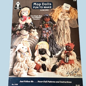 May include: A book cover titled "Mop Dolls FUN TO MAKE" by Judy Askins, featuring several handmade mop dolls. The dolls are crafted from yarn and fabric, showcasing various characters. The cover includes the text "Turn Simple Mops Into Delightful Charmers!"