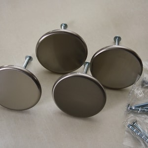 May include: Four round, silver-toned cabinet knobs with screws. The knobs are smooth and have a slightly raised edge. The screws are packaged in a clear plastic bag.