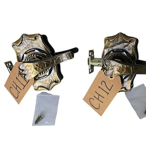 May include: Two antique brass door handles with ornate leaf and web designs. Each handle has a lever and a decorative backplate. The handles have tags labeled "CH11" and "CH12". Small packets of screws are included.
