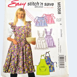 Peut inclure: Un patron de couture McCall's intitulé "Easy stitch'n save" M5358. Le patron présente des modèles de tabliers avec des volants et des poches. La couverture montre une femme portant un tablier floral et des illustrations de différents styles de tabliers.