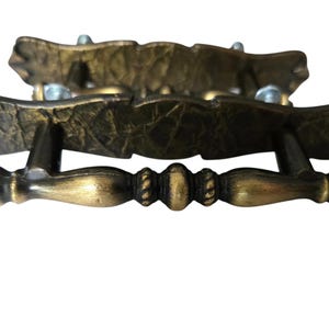 May include: Two antique-style drawer pulls with a textured, dark brass finish. The pulls have a decorative, ornate design with a curved top and a handle with a rope-like detail. Hardware for installation is included.