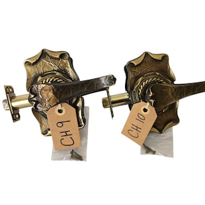 May include: Two antique brass door handles with a leaf design. Each handle has a lever and a backplate. The handles are labeled with tags that read "CH 9" and "CH 10".