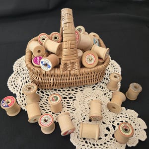May include: A wicker basket overflowing with wooden spools of thread, some with colorful labels, sits on a white lace doily. Several loose spools are scattered around the doily, creating a vintage sewing theme.