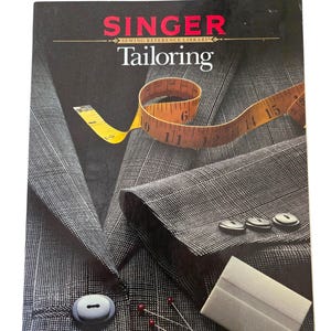 May include: A Singer Sewing Reference Library book titled "Tailoring" with a black cover. The cover features a gray suit jacket, a yellow measuring tape, buttons, pins, and a white sewing tool.
