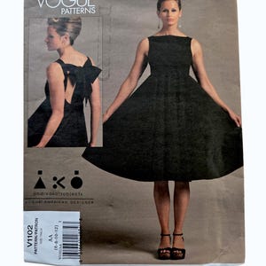May include: Vogue Patterns sewing pattern V1102. The pattern features a black dress with a square neckline and a full skirt. The pattern includes a back view of the dress with a large bow. The pattern is designed by Andrea Katz.