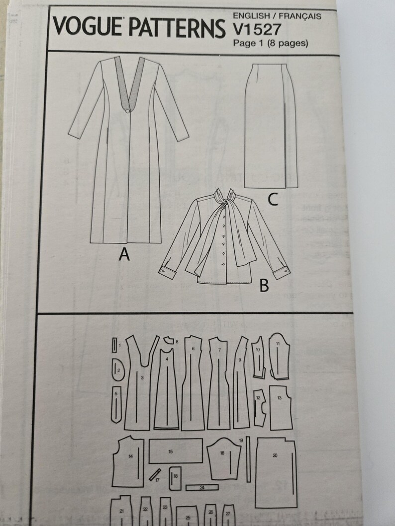 May include: A Vogue Patterns sewing pattern, V1527, featuring illustrations of a long coat, a blouse with a necktie, and a skirt. The pattern also includes diagrams of the pattern pieces. The text "ENGLISH/FRAN&Ccedil;AIS" is visible.
