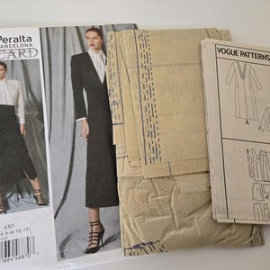 May include: A collection of sewing patterns, including a Vogue Patterns V1527 pattern and a Paco Peralta Barcelona Discard pattern. The patterns feature illustrations of a long coat, skirt, and jacket. The patterns are beige and white.