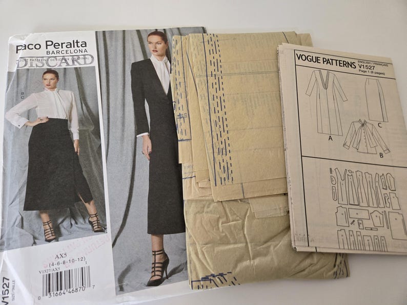 May include: A collection of sewing patterns, including a Vogue Patterns V1527 pattern and a Paco Peralta Barcelona Discard pattern. The patterns feature illustrations of a long coat, skirt, and jacket. The patterns are beige and white.