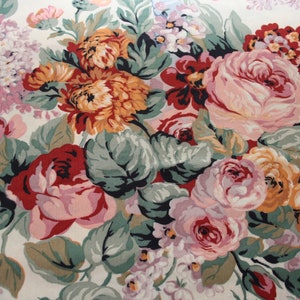 May include: A fabric featuring a dense floral pattern on a cream background. The design includes large clusters of roses and chrysanthemums in shades of deep red, soft pink, orange, and yellow, accented by sage green leaves and small purple flowers.