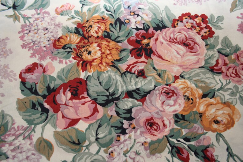 May include: A fabric featuring a dense floral pattern on a cream background. The design includes large clusters of roses and chrysanthemums in shades of deep red, soft pink, orange, and yellow, accented by sage green leaves and small purple flowers.