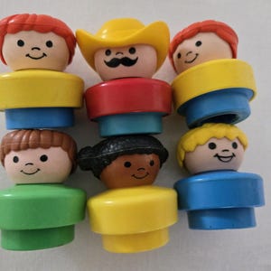 May include: A selection of vintage Fisher-Price Little People figures. The figures have smiling faces and are dressed in various colours, including yellow, red, blue, and green. One figure wears a yellow cowboy hat.