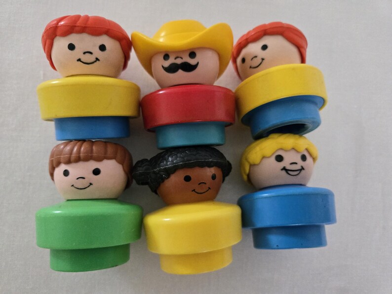 May include: A selection of vintage Fisher-Price Little People figures. The figures have smiling faces and are dressed in various colours, including yellow, red, blue, and green. One figure wears a yellow cowboy hat.
