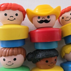 May include: A collection of vintage Little People figures. The figures have smiling faces and are stacked. The figures have yellow, red, blue, green, and brown components. One figure wears a yellow cowboy hat and has a black moustache.