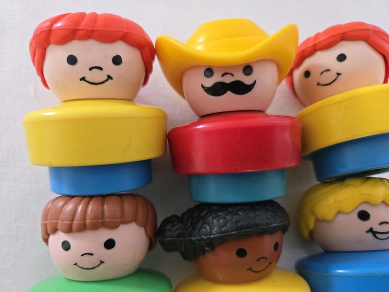 May include: A collection of vintage Little People figures. The figures have smiling faces and are stacked. The figures have yellow, red, blue, green, and brown components. One figure wears a yellow cowboy hat and has a black moustache.
