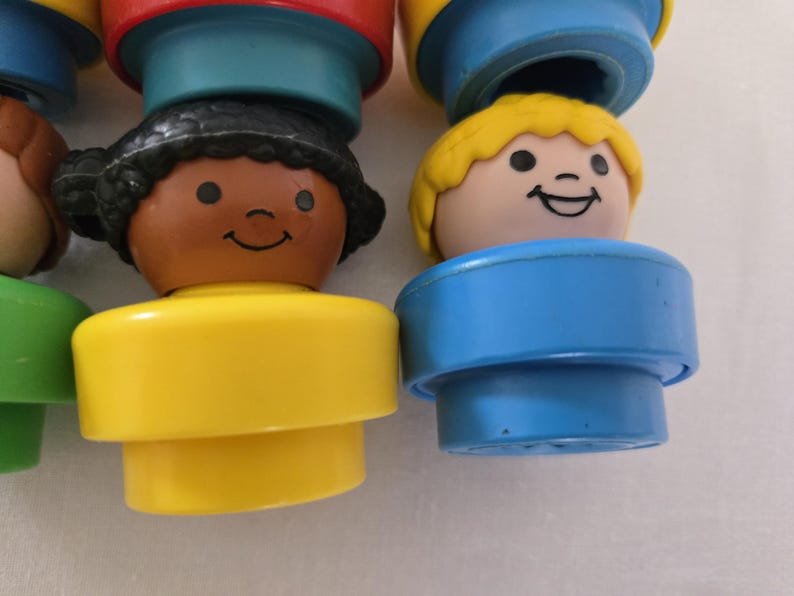 May include: Close-up of several vintage Fisher-Price Little People figures. The figures have smiling faces, with yellow, brown, and black hair. The figures have yellow, blue, and green bases. The figures are a classic toy.