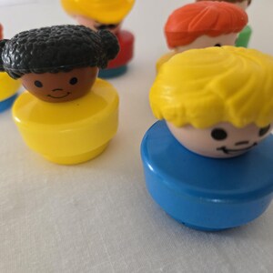 May include: A selection of colourful, vintage toy figures. The figures have round bodies in yellow and blue, with smiling faces and different coloured hair, including red, yellow, and black. These classic toys are reminiscent of childhood.