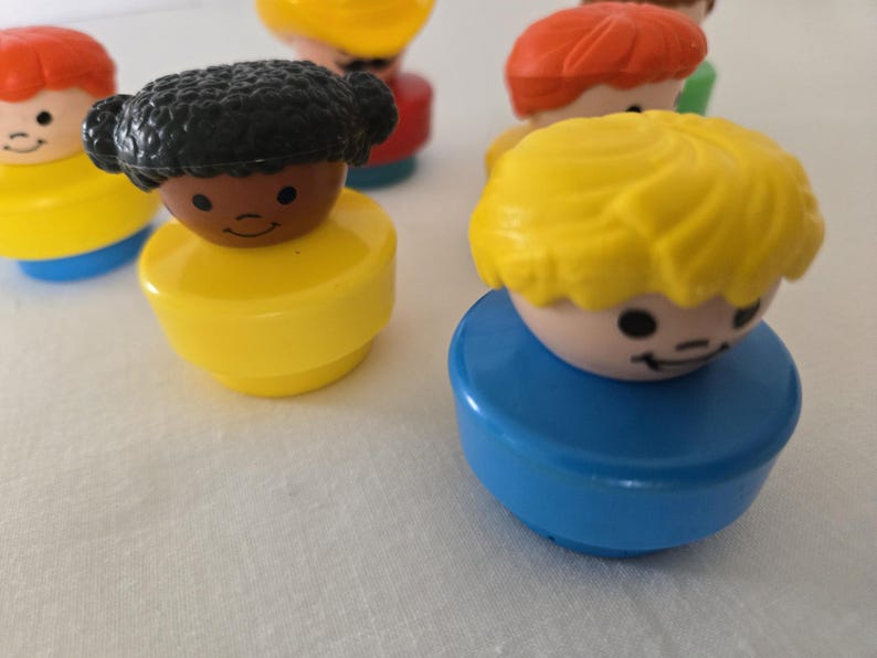 May include: A selection of colourful, vintage toy figures. The figures have round bodies in yellow and blue, with smiling faces and different coloured hair, including red, yellow, and black. These classic toys are reminiscent of childhood.