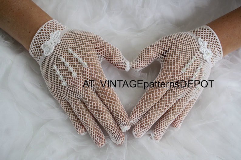 May include: A pair of white mesh gloves with pearl embellishments and a floral design. The gloves are held together in a heart shape.