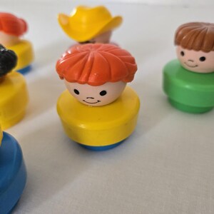 May include: A selection of vintage Fisher-Price Little People figures. The figures have different hair colours, including red, brown, and black, and are wearing various coloured outfits. One figure is wearing a yellow cowboy hat.
