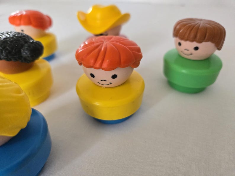 May include: A selection of vintage Fisher-Price Little People figures. The figures have different hair colours, including red, brown, and black, and are wearing various coloured outfits. One figure is wearing a yellow cowboy hat.