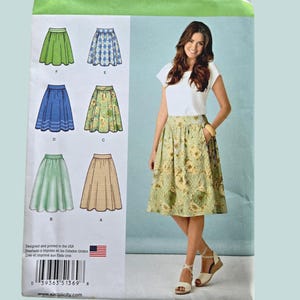May include: Simplicity sewing pattern 1369 H5 showing different skirt designs. The package features a woman wearing a floral skirt. The pattern includes skirt styles in green, blue, and tan. The text "Designed and printed in the USA" is visible.