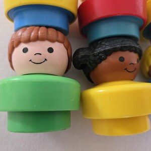 May include: Close-up of several colourful, vintage toy figures. Each figure has a smiling face and a different hair colour, including brown, black, and blonde. The figures are stacked on top of each other, with a variety of bright colours.